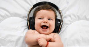Bebê sorridente usando fones de ouvido grandes, deitado sobre um colchão branco