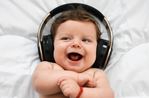Bebê sorridente usando fones de ouvido grandes, deitado sobre um colchão branco