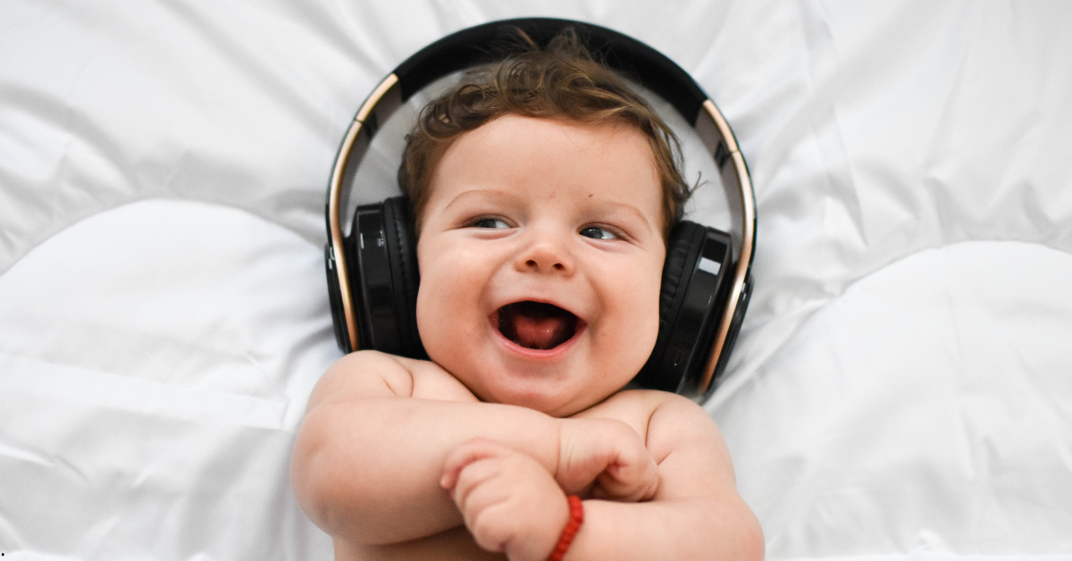 Bebê ouvindo música com fones de ouvido na rotina diária Bebê sorridente usando fones de ouvido grandes, deitado sobre um colchão branco