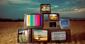 TVs antigas empilhadas em um campo seco, exibindo imagens coloridas e estáticas