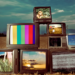 TVs antigas empilhadas em um campo seco, exibindo imagens coloridas e estáticas