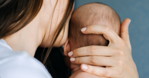 Mãe segurando o bebê com carinho enquanto olha para baixo, demonstrando emoção