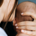 Mãe segurando o bebê com carinho enquanto olha para baixo, demonstrando emoção