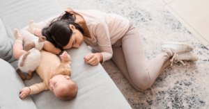 Mãe deitada ao lado do bebê no chão, ambos exaustos