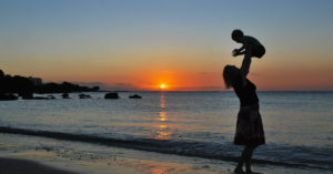 Mãe solo brincando com seu filho na praia ao pôr do sol