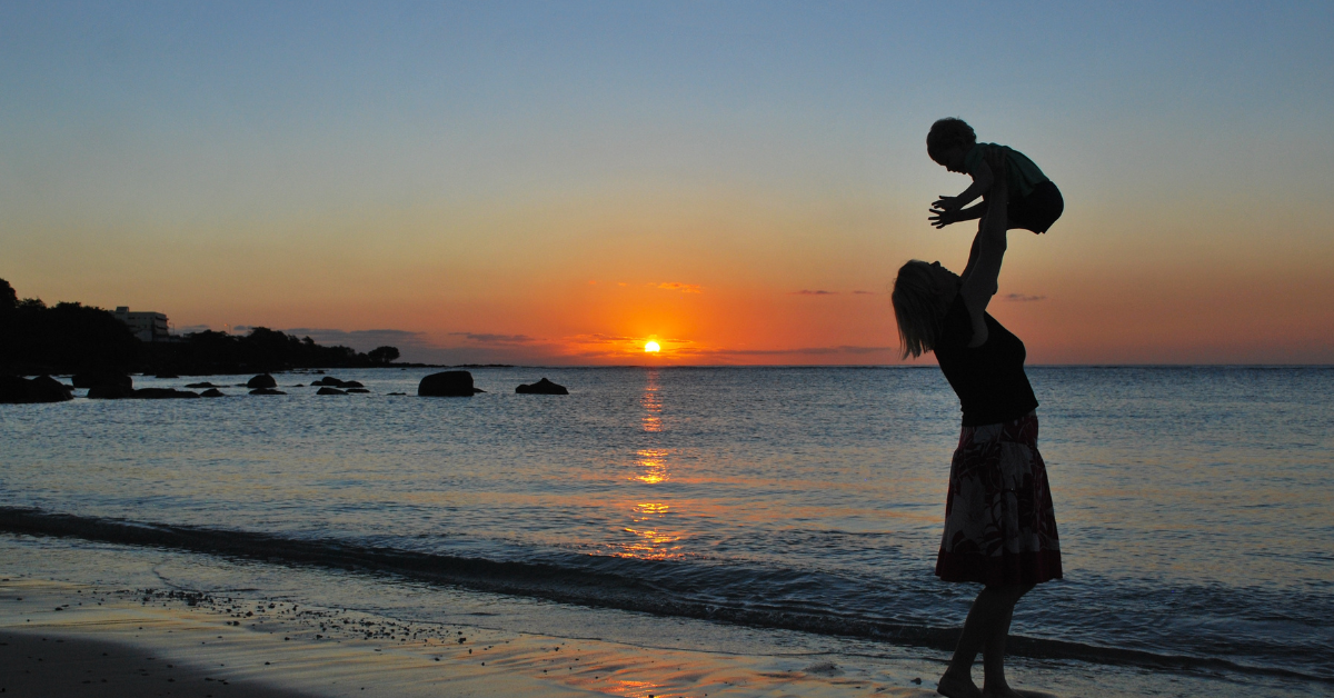 Mãe solo brincando com seu filho na praia ao pôr do sol