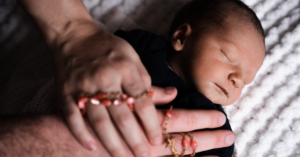 Bebê dormindo durante a regressão do sono, com mãos adultas oferecendo conforto e acolhimento
